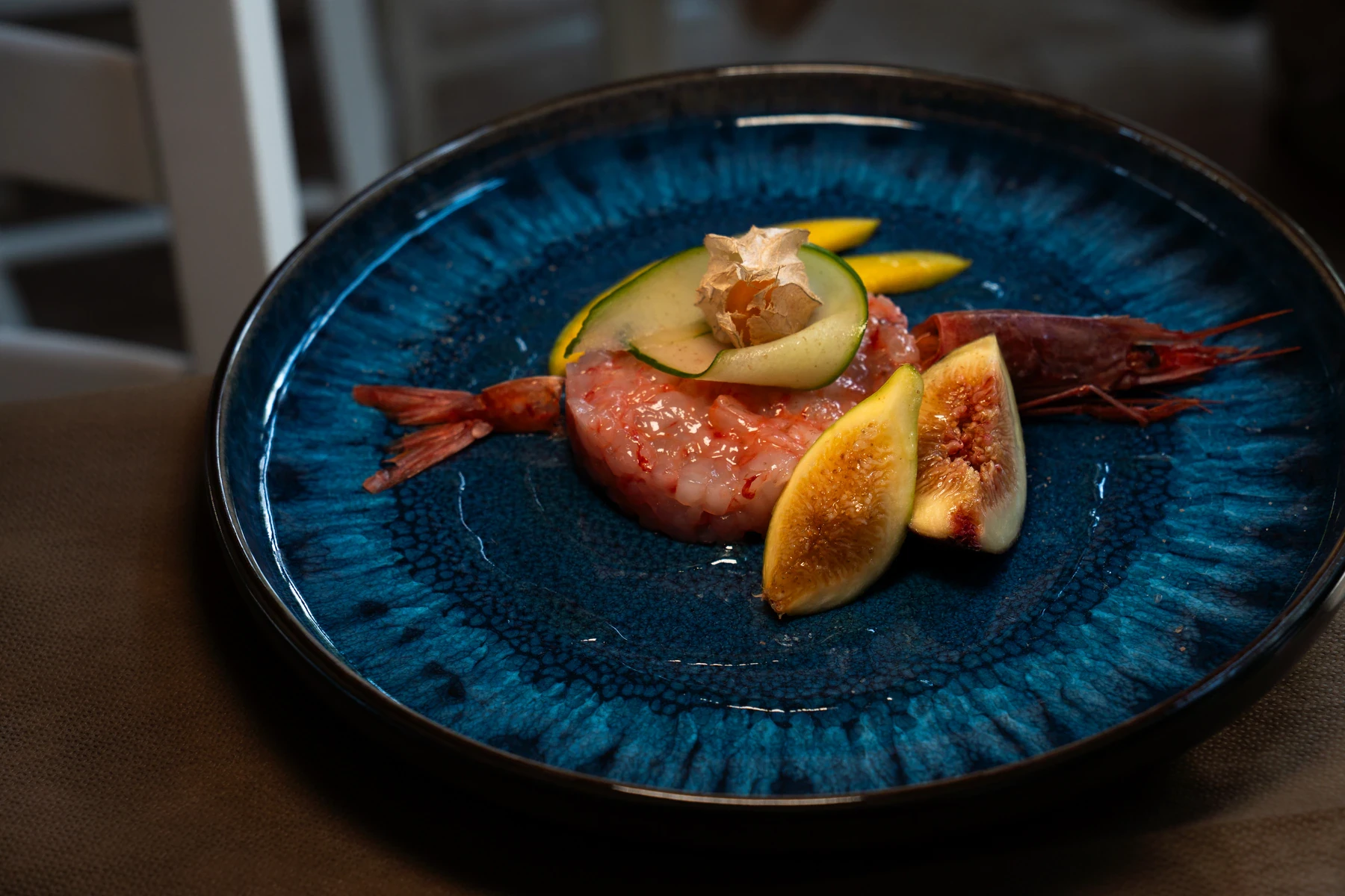 Tartare di gambero rosso servita su un piatto blu con fichi freschi e delicate guarnizioni vegetali