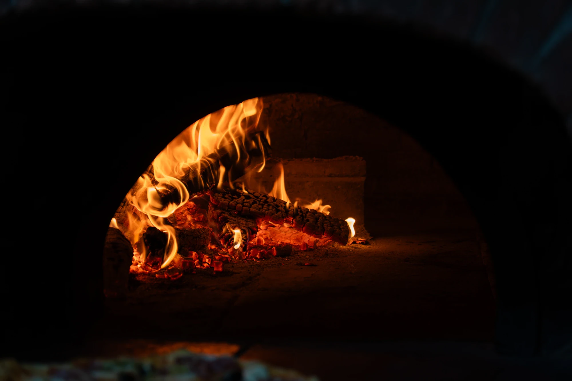 Interno del forno a legna di Le Mimose con fiamme e braci ardenti