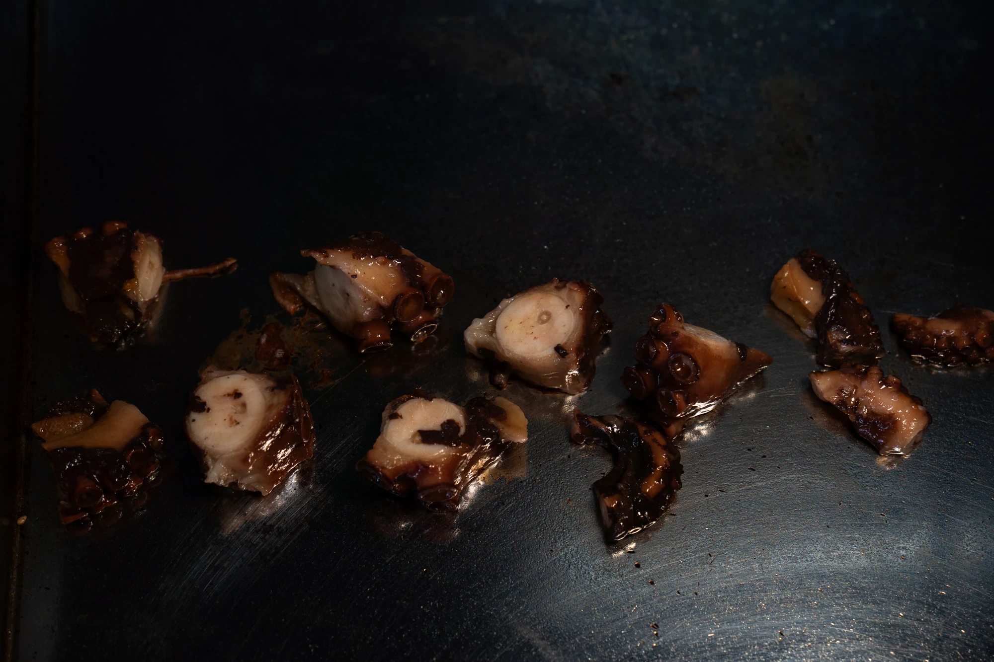 Pezzi di polpo grigliato su una piastra metallica scura della cucina